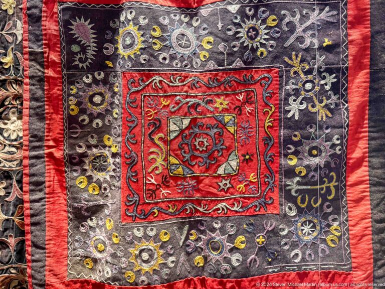 Square dark textile with central red medallion.