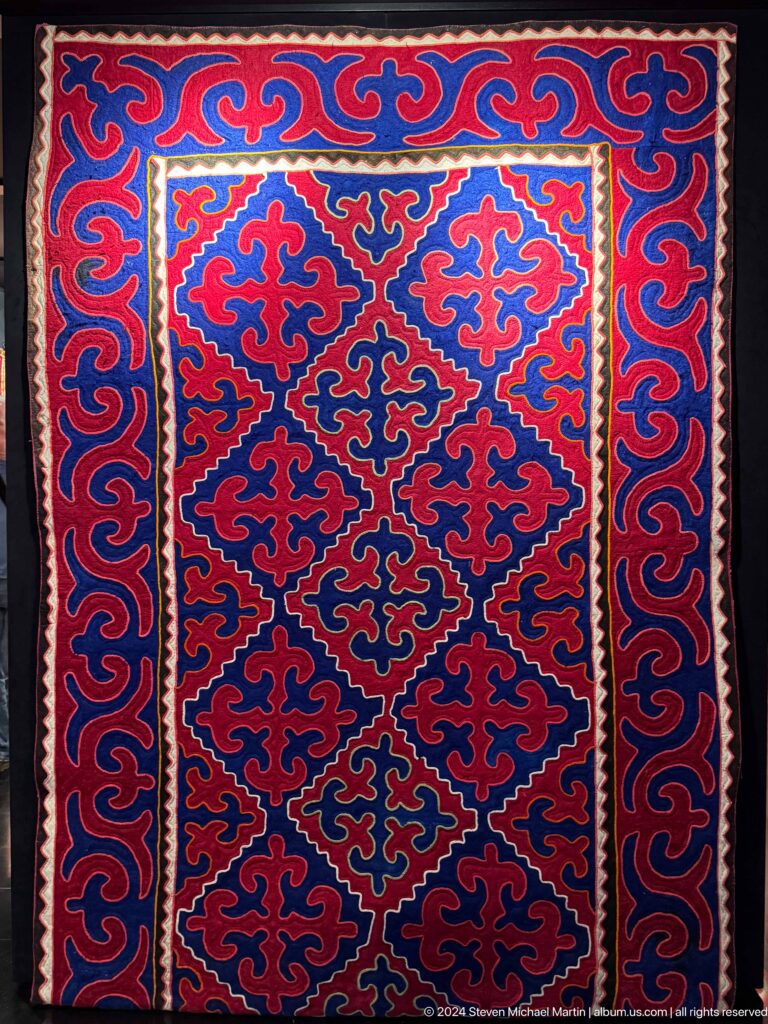 Blue and red felt carpet with repeated horn motifs.
