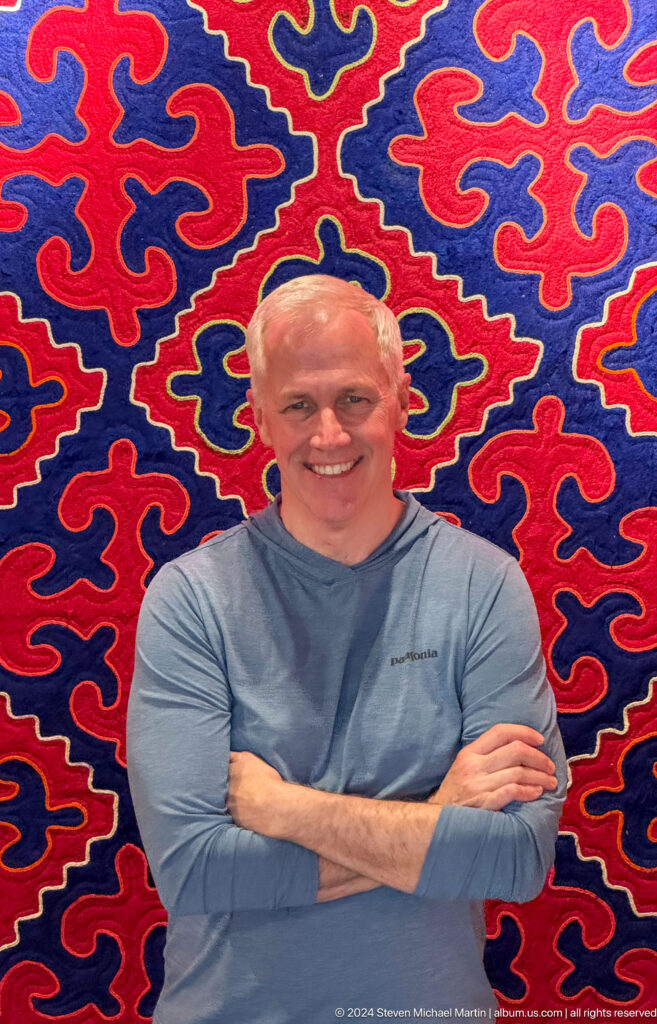 Smiling male visitor posed before red and blue felt carpet.