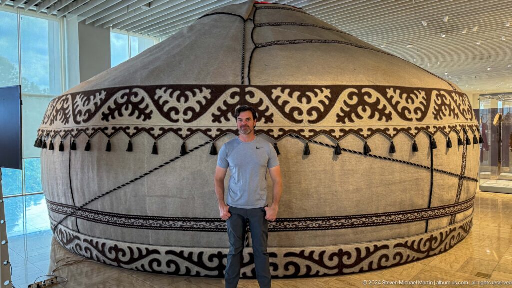 Male visitor standing beside a large yurt interior display.