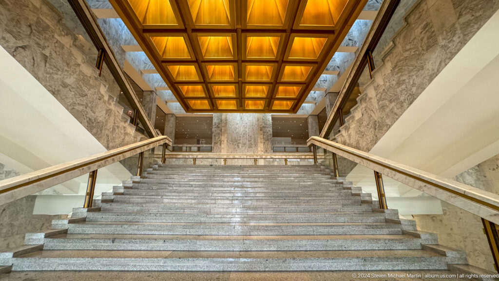 Grand marble staircase beneath glowing coffered ceiling.