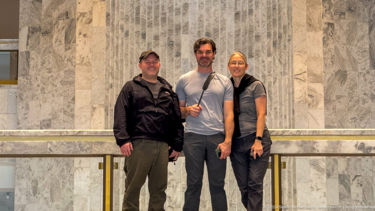 Three visitors posing in front of monumental marble relief.