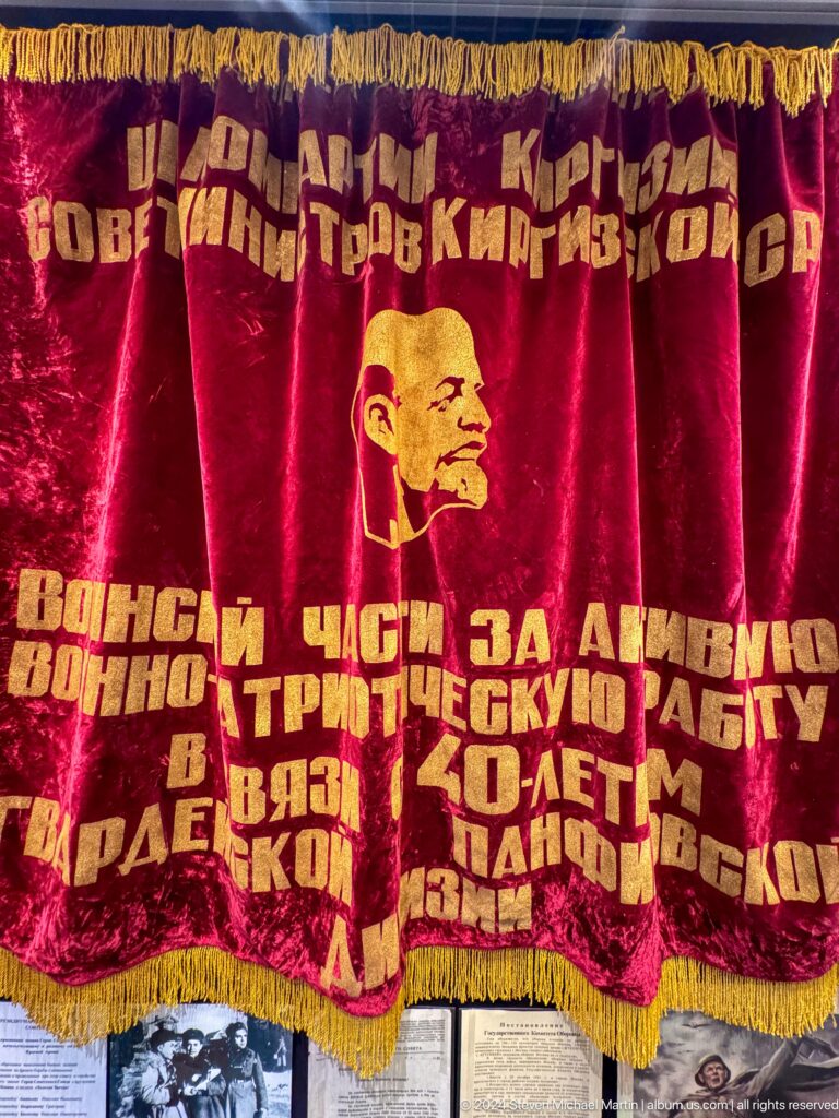Red velvet banner with Lenin portrait and Cyrillic slogan.