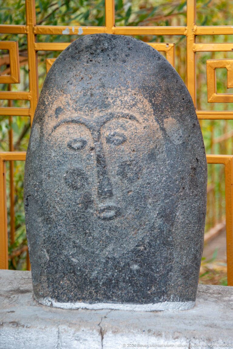 A weathered stone head preserves a broad face with simplified eyes, nose, and mouth