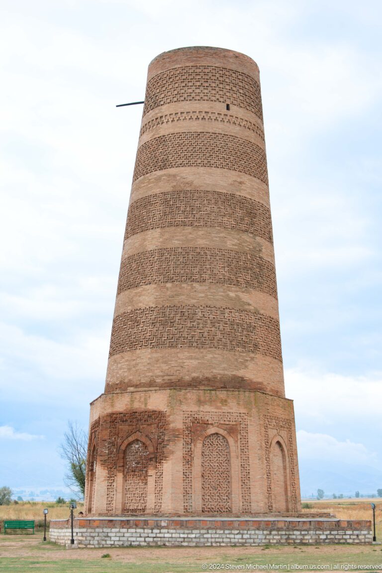 The tapering cylindrical brick shaft rises against a cloudy sky