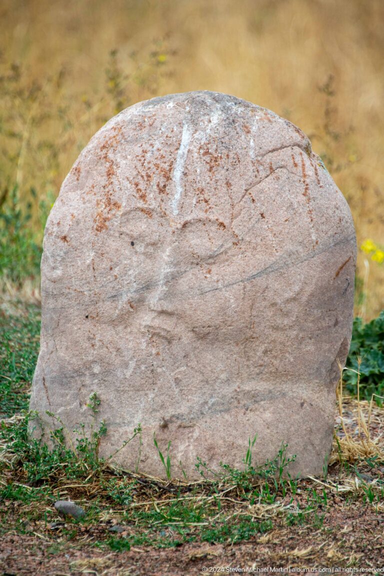 A standing stone figure retains facial features and a faintly carved torso