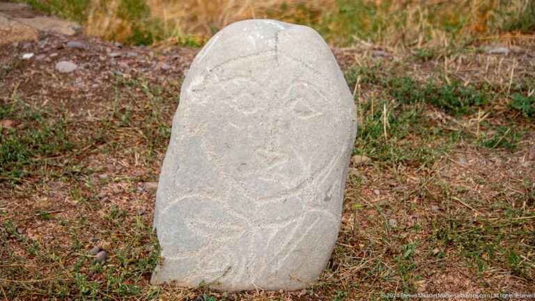 An oval stone figure carries a stylized face and looping incised decoration