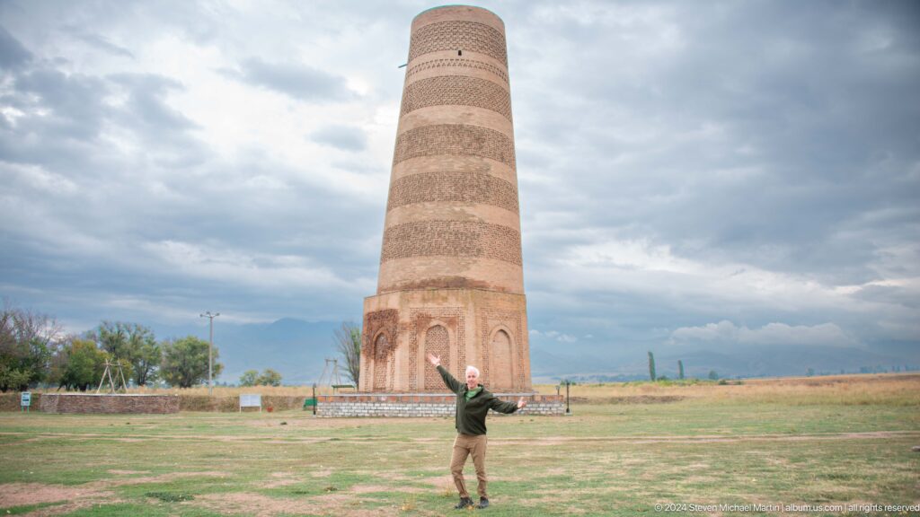 A visitor stands with arms raised before the distant minaret