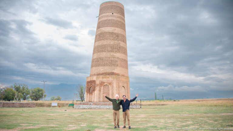 Two visitors raise their arms in a playful pose with the tower centered behind them