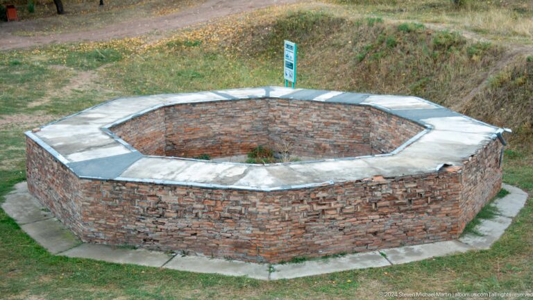 A low circular brick foundation or reconstructed feature lies within the site