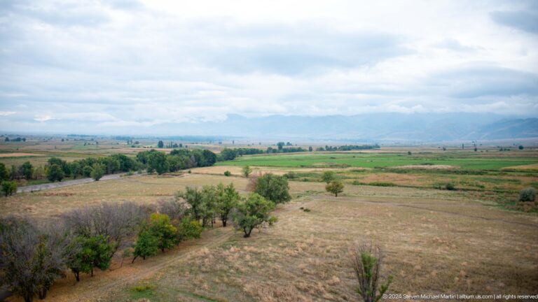 Patchwork fields, trees, and distant mountains spread beyond the archaeological site