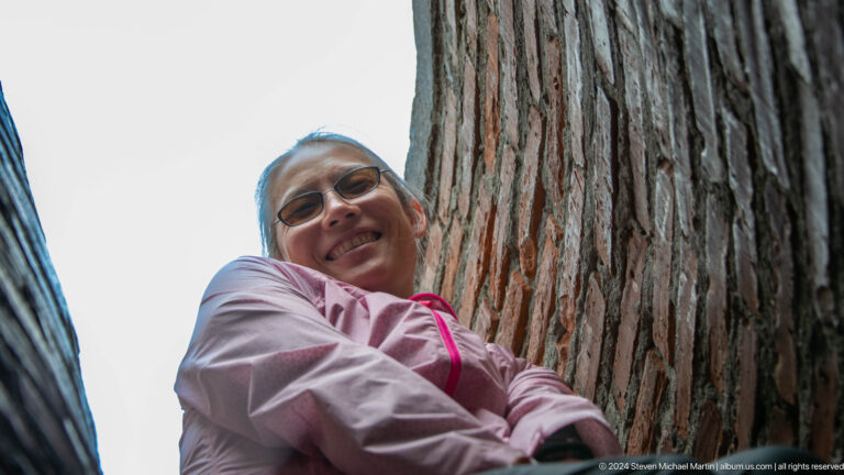 A visitor wearing glasses looks toward the camera from the narrow brick shaft