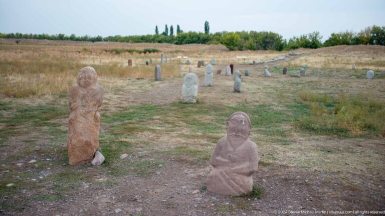 Several carved Turkic stone figures stand across the archaeological landscape