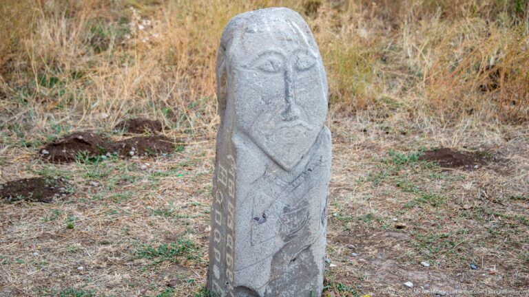 A standing stone figure shows an elongated face and hands held before the body
