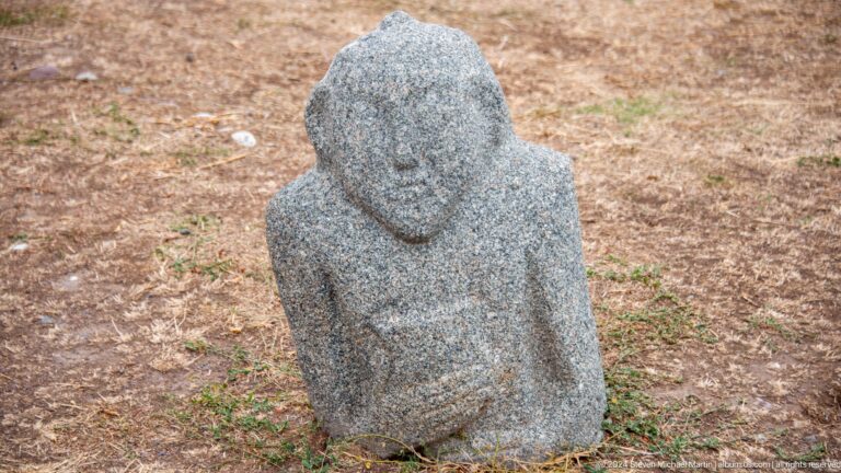 A squat weathered figure appears seated with folded arms