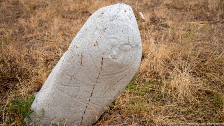 A light-colored stone figure bears a simple incised face and weathered surface