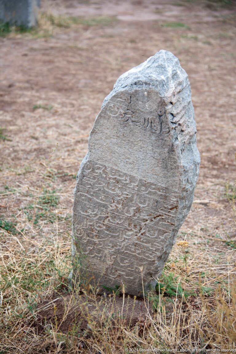 A dark upright stone carries dense flowing Arabic-script inscription
