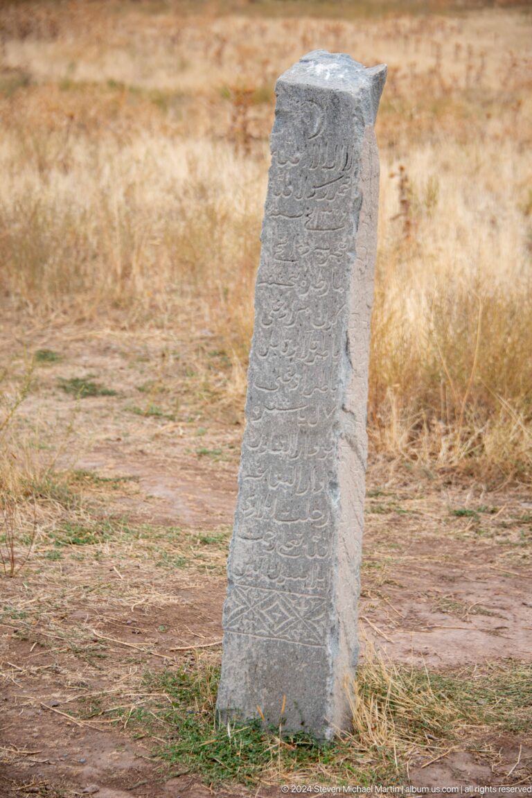A slender stone marker bears vertically arranged Arabic-script carving