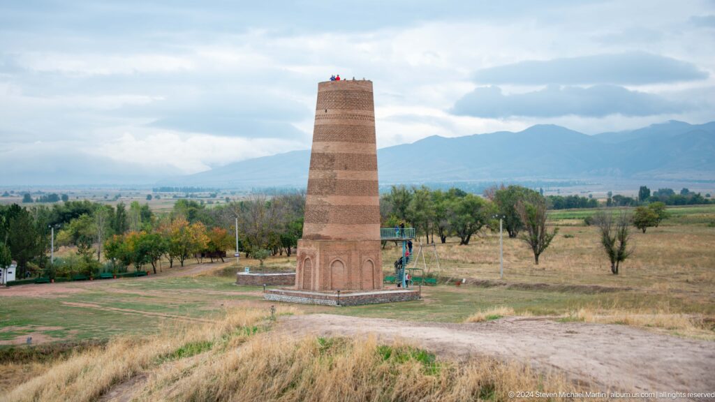 The tower stands within its archaeological grounds against distant mountains