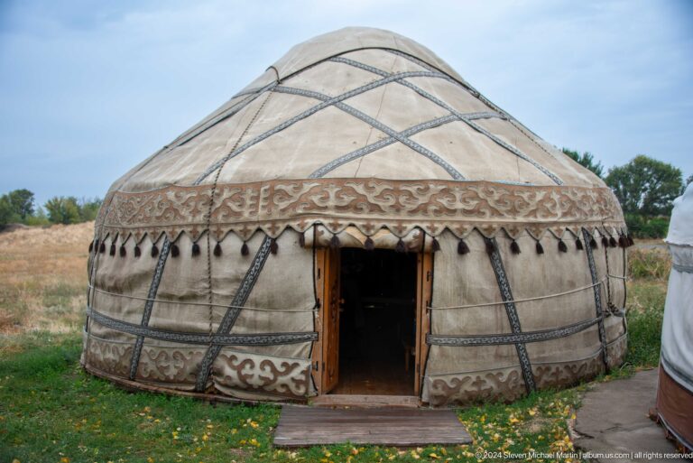 A felt-covered circular yurt displays patterned bands and a dark central doorway