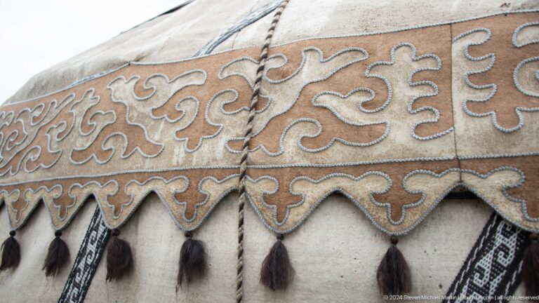 Cream and tan felt motifs form scrolling patterns above hanging tassels