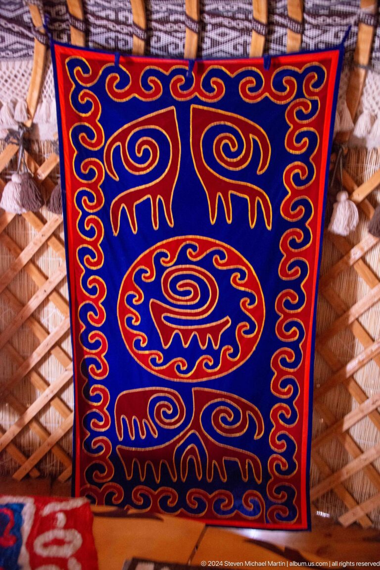 A vivid square panel contains a central spiral animal-like motif within a red border