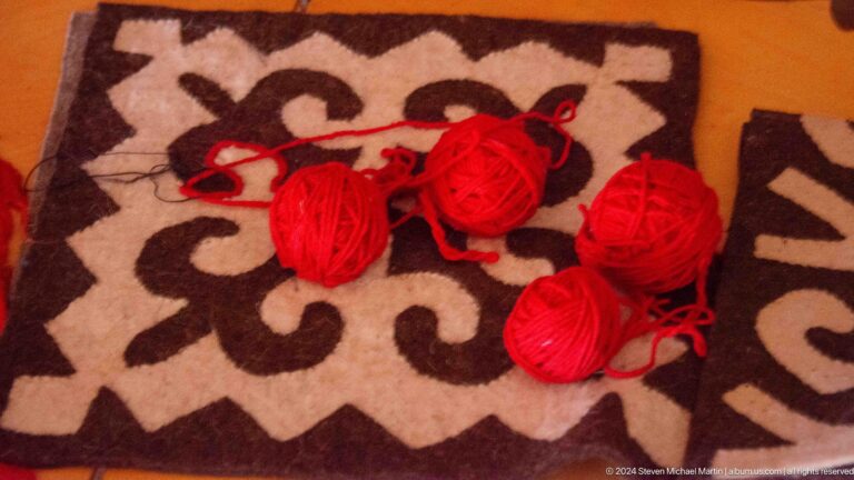 Balls of red yarn lie on a patterned felt surface during textile work