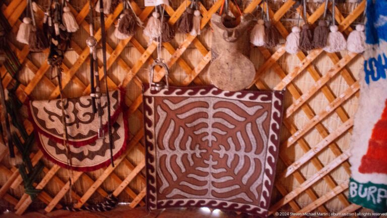 A dark hanging bag with pale radiating ornament is mounted against the lattice wall