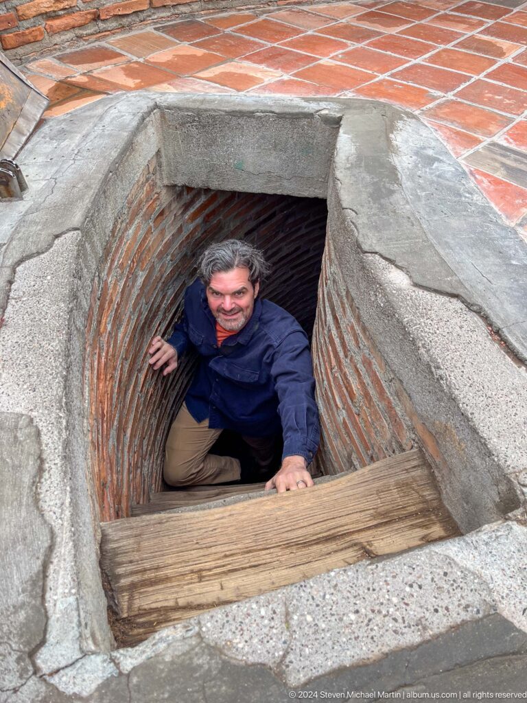 A visitor climbs through a narrow brick opening at the top of the stair passage