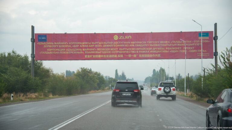 Cars passing beneath a long roadside banner.
