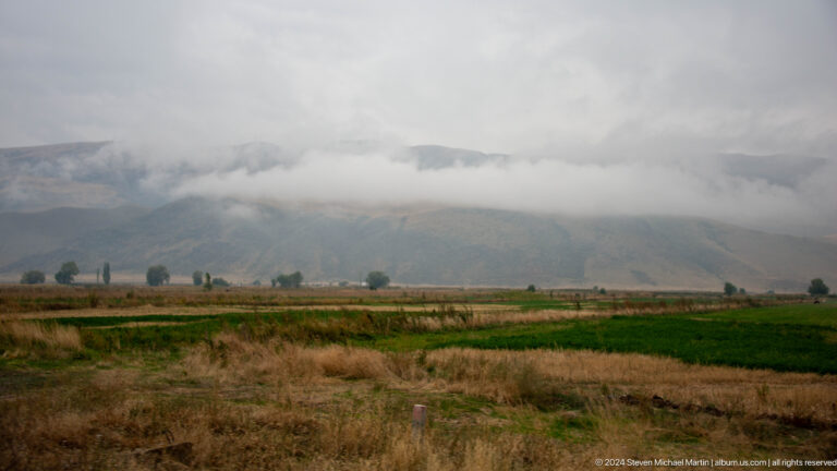 Farmland under low clouds and mountain foothills.