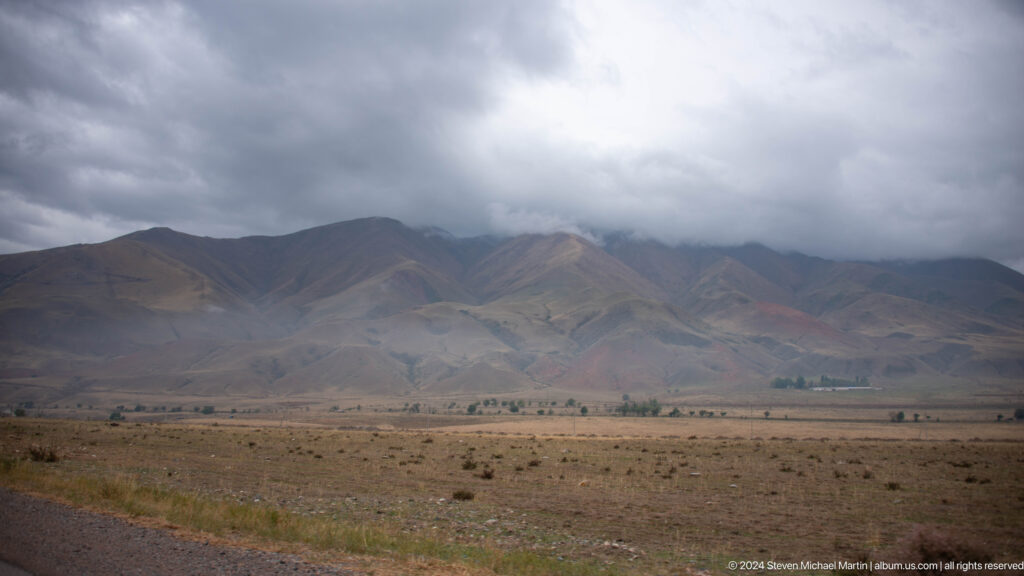 Barren valley beneath dark cloud-covered mountains.