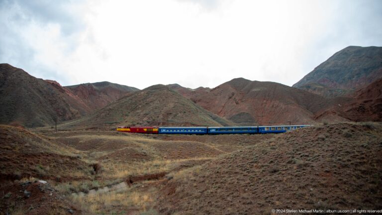 Long blue passenger train crossing barren hills.