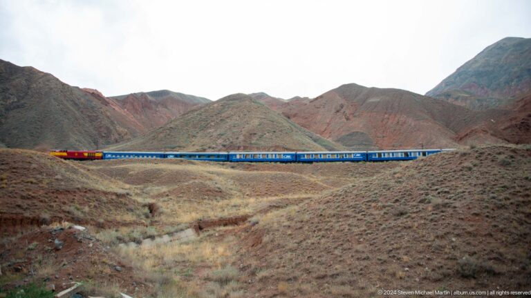Blue train stretching across reddish hills.