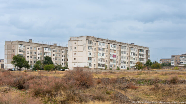 Soviet-era apartment blocks beyond dry grass.