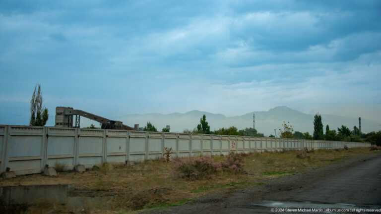 Long walled compound beneath cloudy mountains.