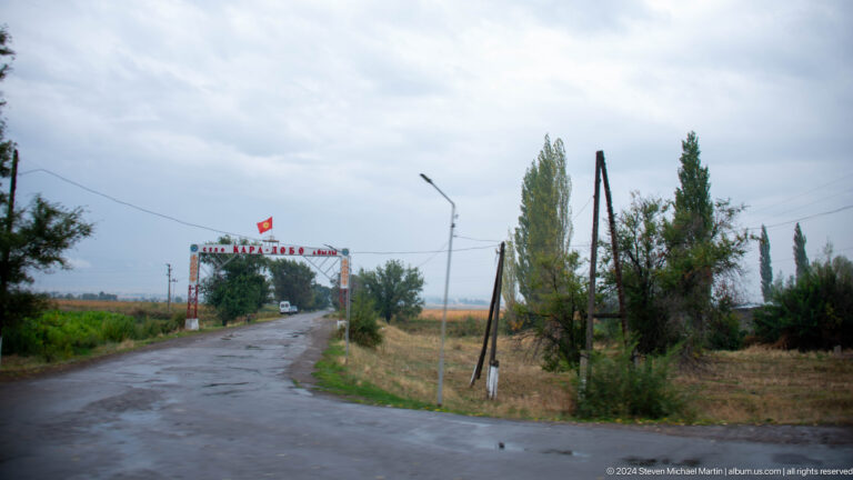 Wet roadside entrance with distant sign.