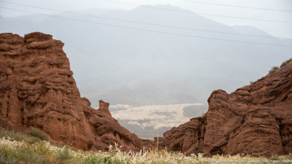 Entrance into a red earthen canyon with hazy valley beyond.