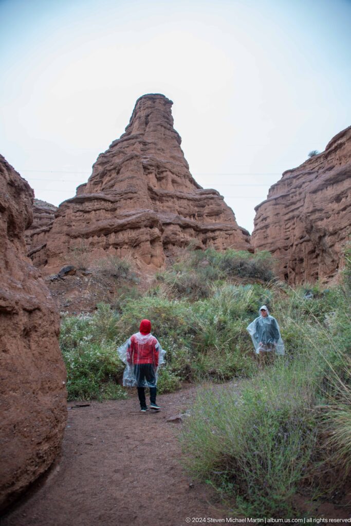 Two visitors walking beneath towering layered canyon walls.