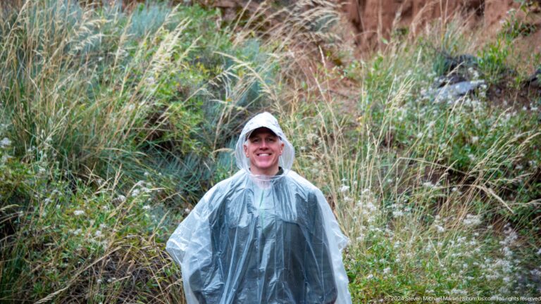 Smiling visitor in clear rain poncho among canyon vegetation.