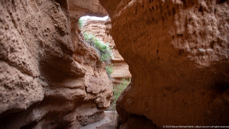 Deep shadowed rock opening framing a green canyon floor.