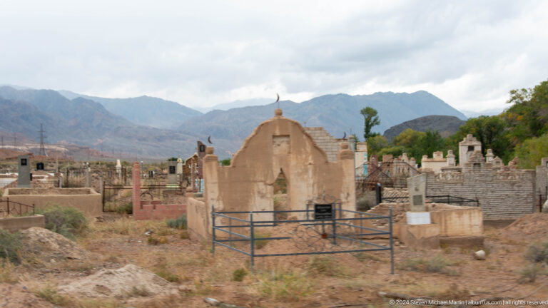 Small cemetery with earth-toned arched grave enclosure and mountains.