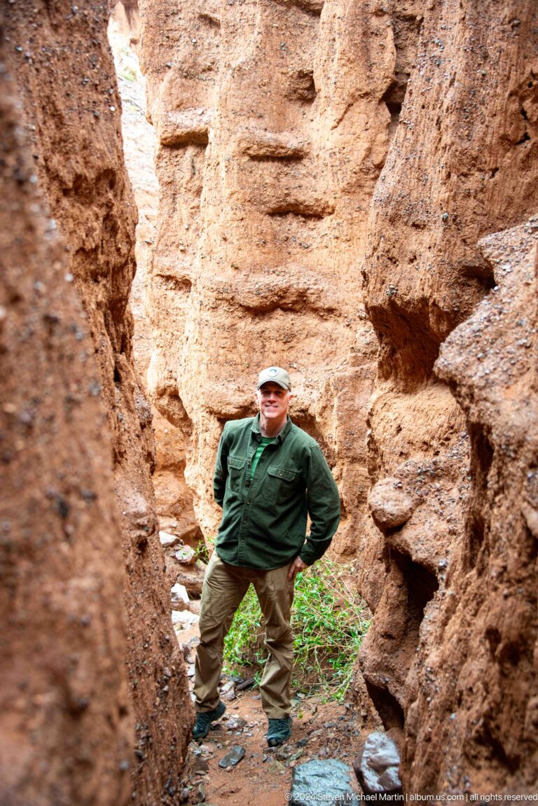Man in green jacket standing beside rounded earthen formations.