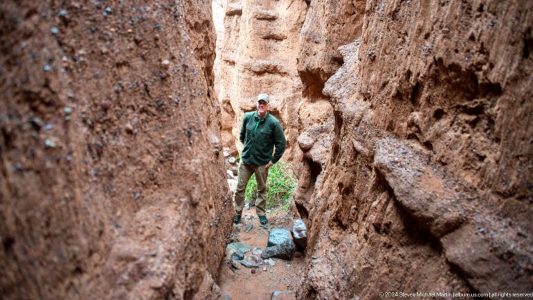 Visitor walking through narrow canyon carrying gear.