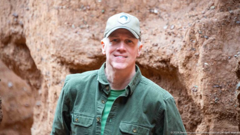 Close smiling portrait of man in green jacket and cap.
