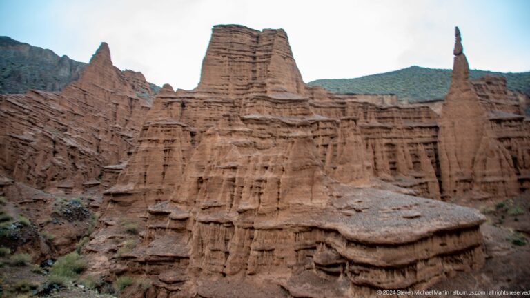 Massive flat-topped red formation with slender spire at right.