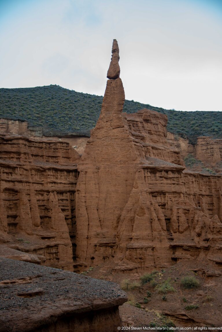 Close view of tall tapering earthen fin against cliff.