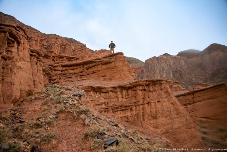 Small figure standing atop red canyon ridge.