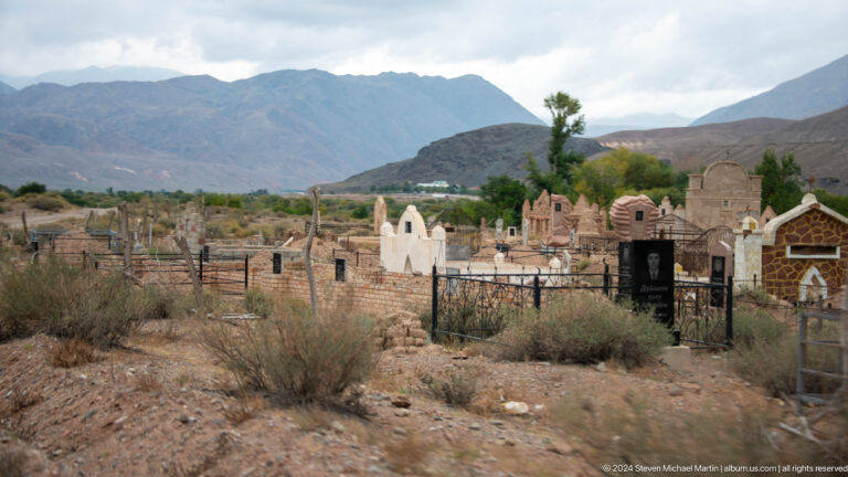 Wide cemetery view with white and brick memorials below mountains.