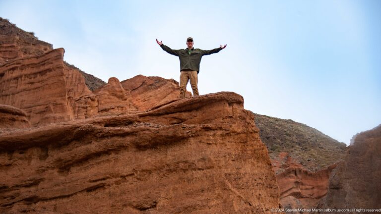 Visitor standing arms outstretched on red ledge.